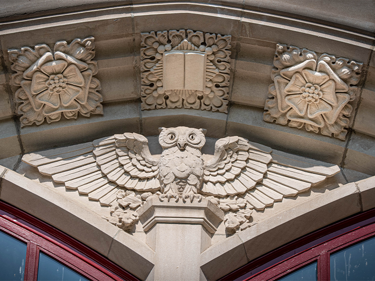 A owl with outstretched wings is carved in stone in the archway of a building.